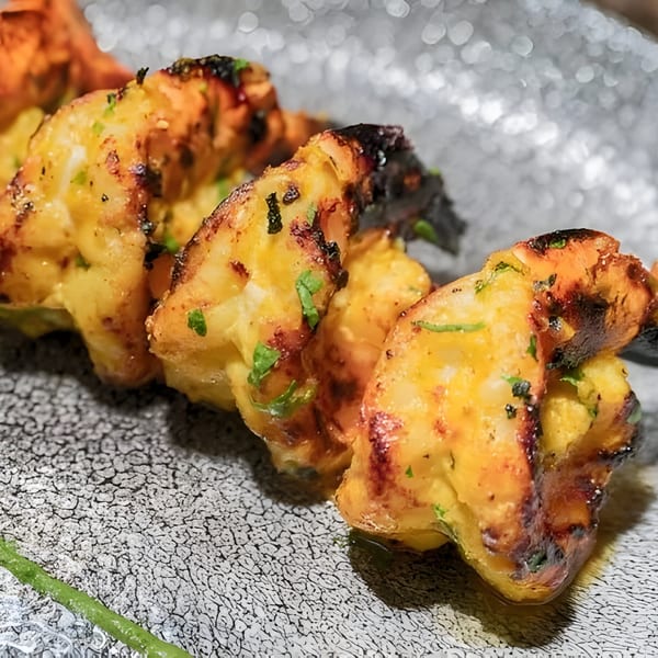 Close-up of grilled Indian shrimp skewers with char marks and green herbs on a textured plate.