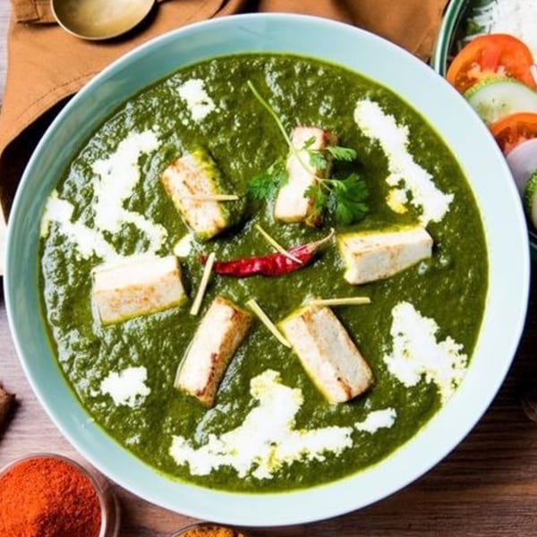 Palak Paneer, a vibrant green Indian dish with paneer cheese, cream, and red chili in a blue bowl.