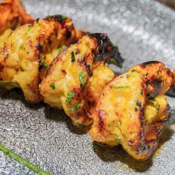 Close-up of grilled Indian shrimp skewers with char marks and green herbs on a textured gray plate.