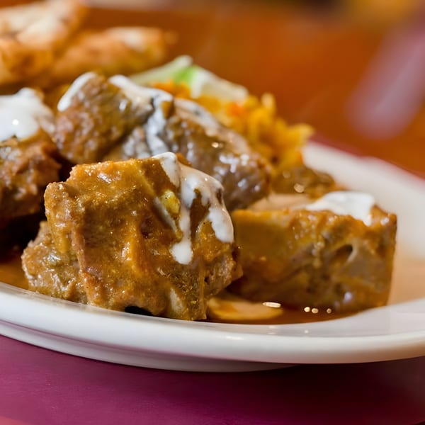 Close-up of Indian curry with meat pieces drizzled with white sauce, served on a white plate.