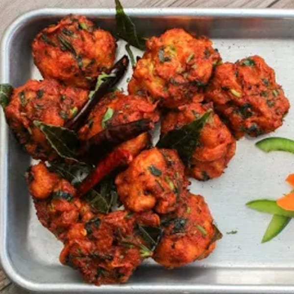 Spice Venue's vibrant red Indian chicken pakora, garnished with curry leaves and chili, on a silver tray.