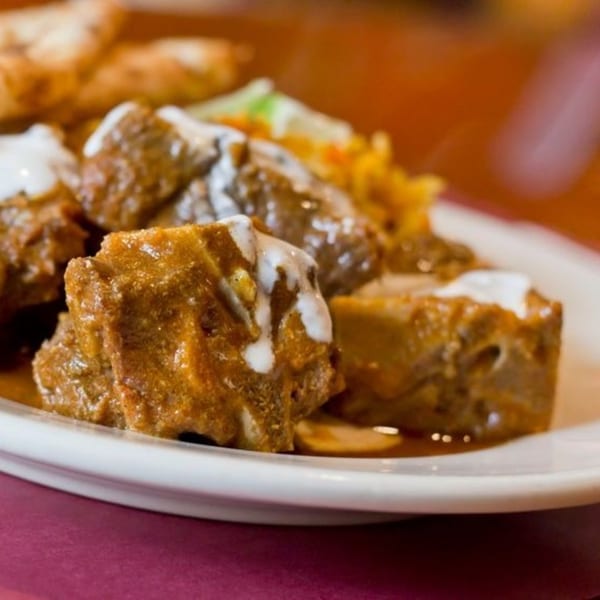Indian curry with meat pieces drizzled with white sauce, served with rice and naan bread.