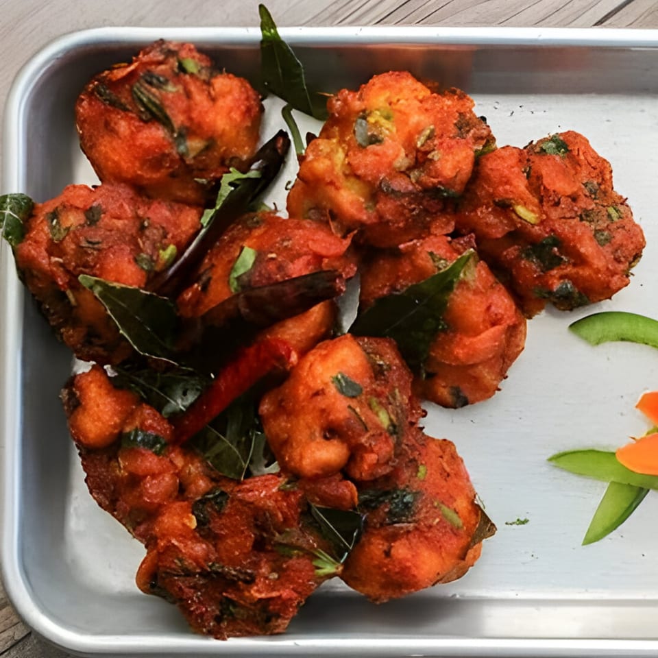 Deep-fried Indian chicken pakora, garnished with curry leaves and red chilies, on a metal tray.