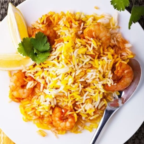 Spice Venue's shrimp biryani, a vibrant Indian dish with yellow and white rice, shrimp, lemon, and cilantro.