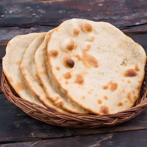 Freshly baked Indian naan bread with golden-brown spots, served in a woven basket on a dark wooden surface.
