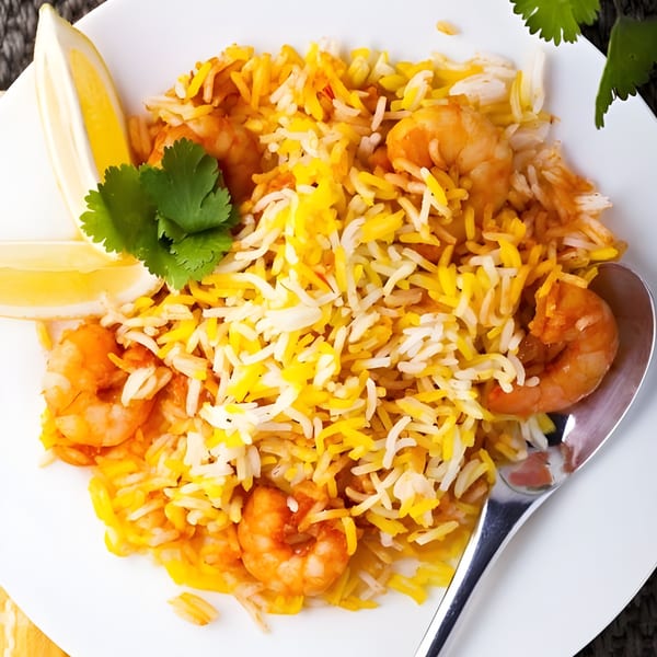 Spice Venue's shrimp biryani with yellow and white rice, garnished with cilantro and lemon wedges.