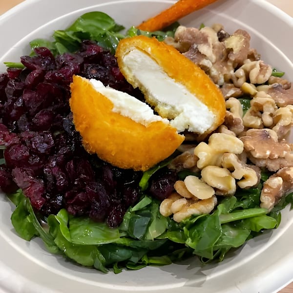 A salad with spinach, dried cranberries, walnuts, and fried goat cheese in a white bowl.